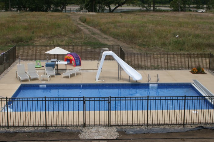 backyard pool with slide, fence, and seating area.
