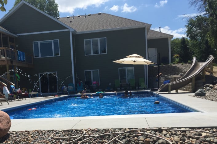backyard pool with kids swimming and slide and deck jets.