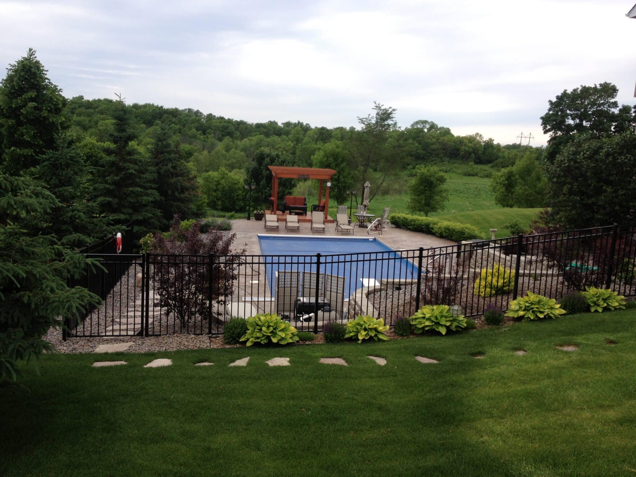A view of a backyard with a swimming pool, patio, and lush green hills in the background.