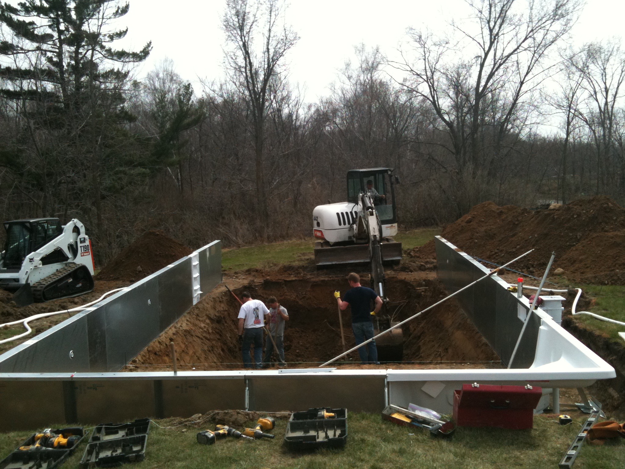 Construction workers and excavators installing an inground swimming pool in a backyard.
